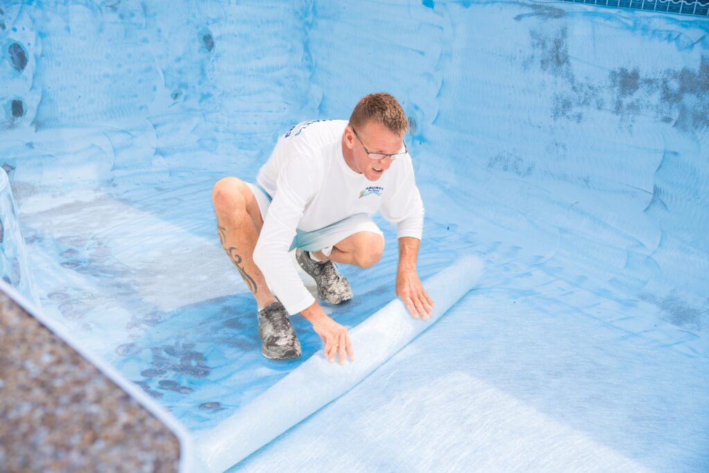 Man applying fiberglass coating in an empty swimming pool, demonstrating fiberglass resurfacing process for improved durability and maintenance.