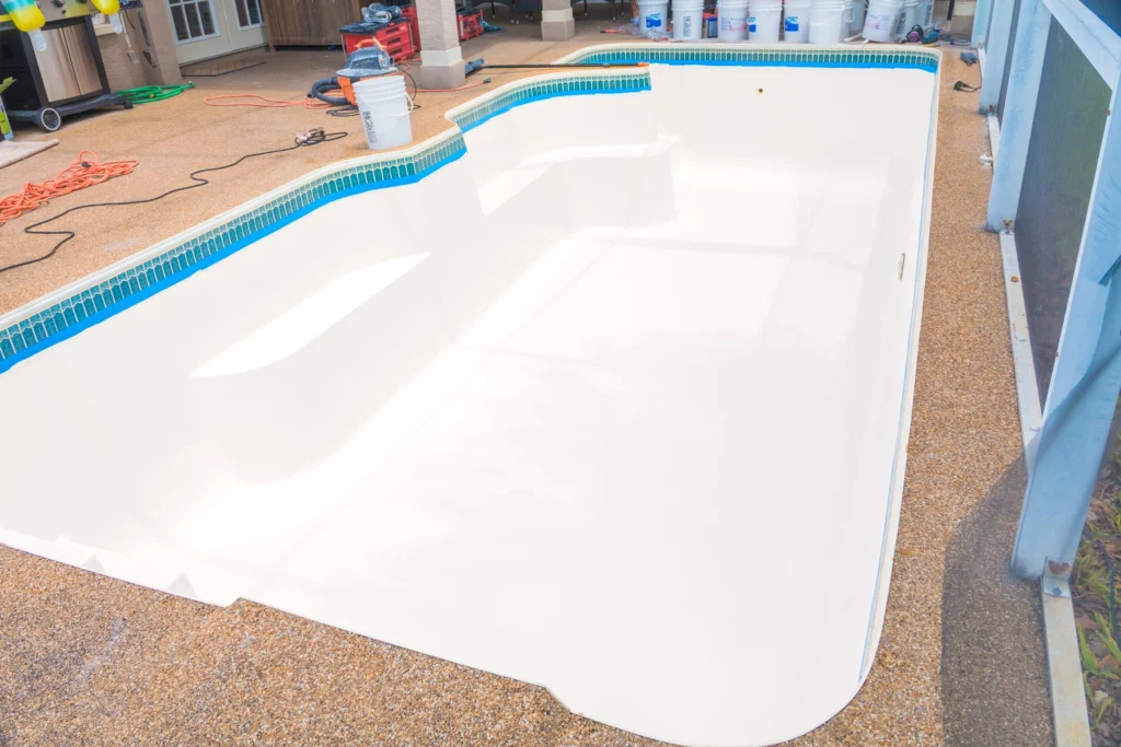 Fiberglass pool with a smooth, white resurfacing finish, showcasing the transformation process, surrounded by tools and materials for pool maintenance.